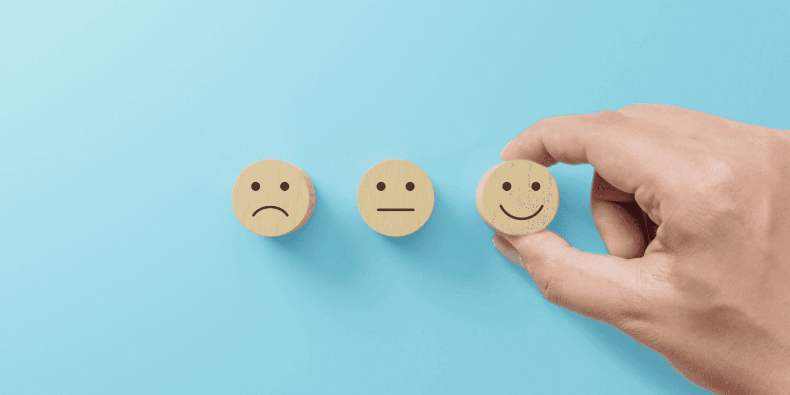 Hand selecting happy face emoji from three sentiment rating options on blue