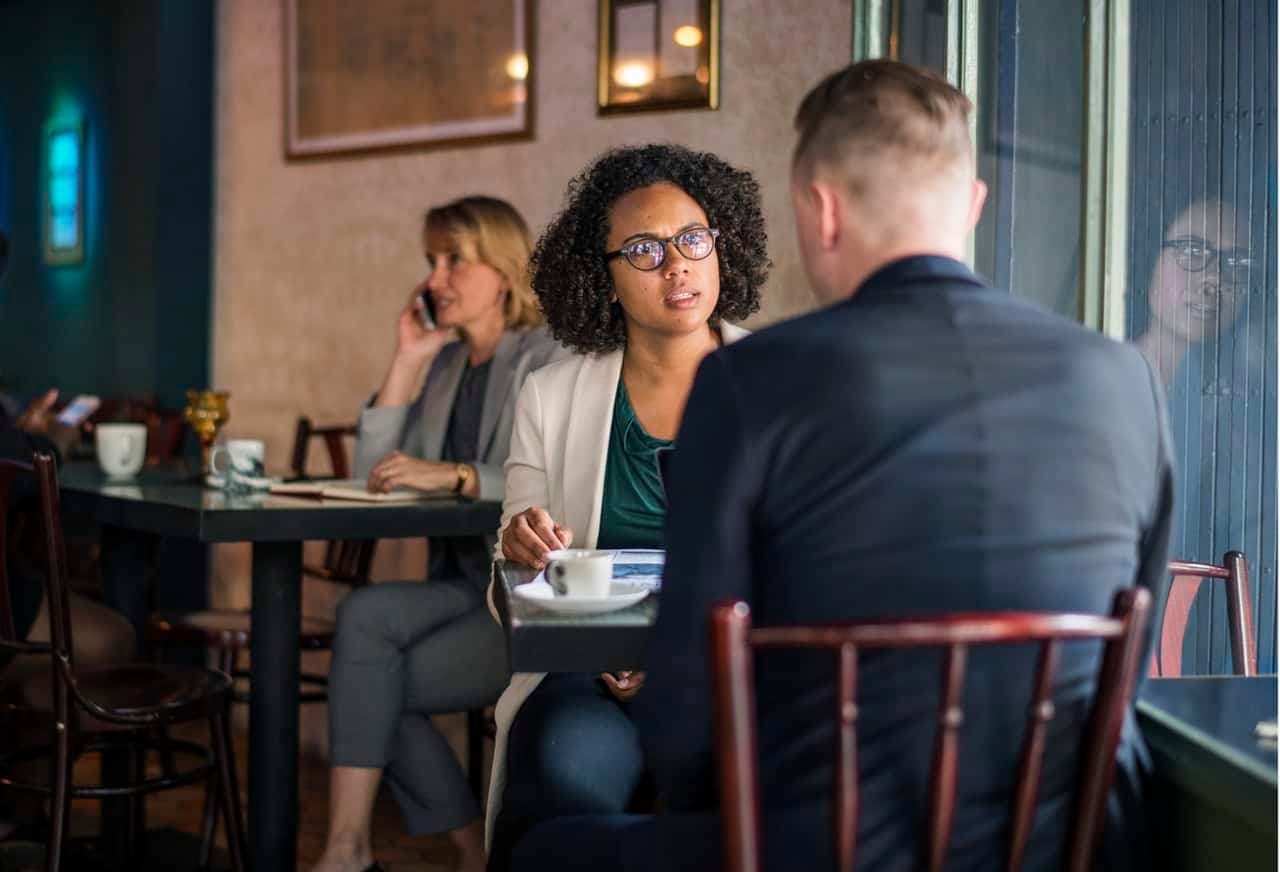Woman in blazer speaking with man in cafe setting