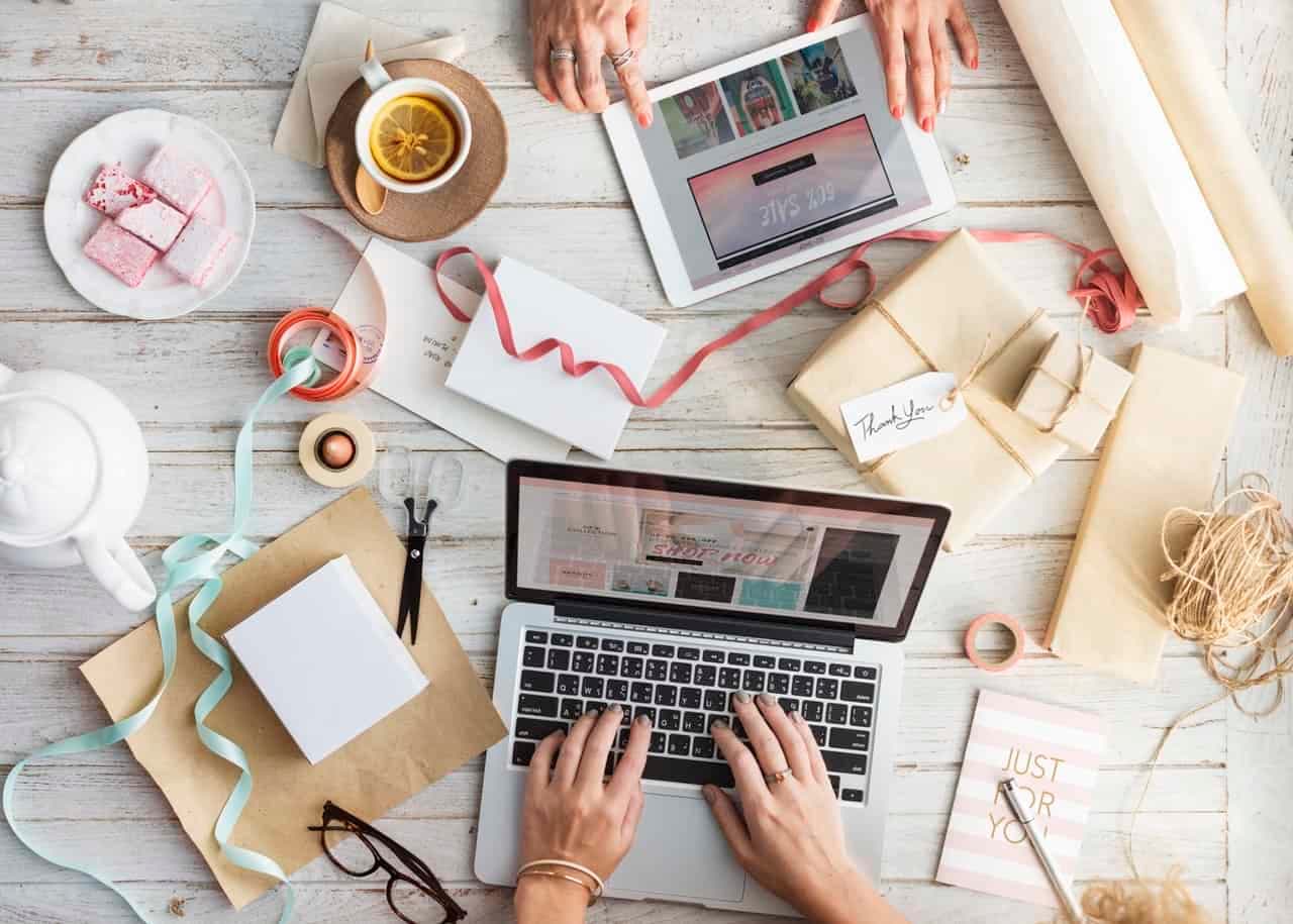 Overhead view of designer workspace with laptop, tablet, design materials, tea, and gift boxes