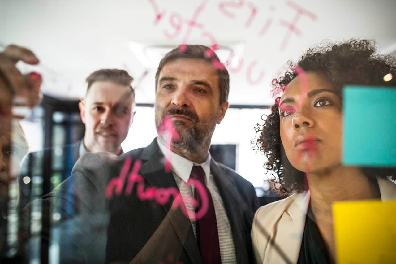 Group of business colleagues brainstorming and writing notes on a glass wall with sticky notes