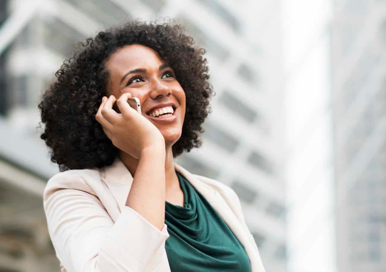 Woman on phone call smiling in business attire with blurred city buildings in background