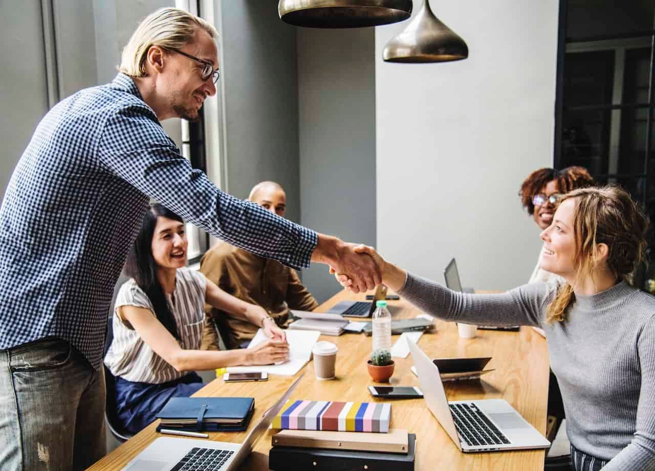 Colleague greeting team members at wooden conference table