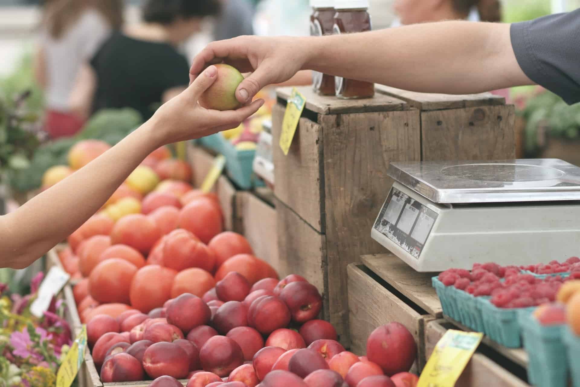 Hand selecting apple at farmers market display with scale