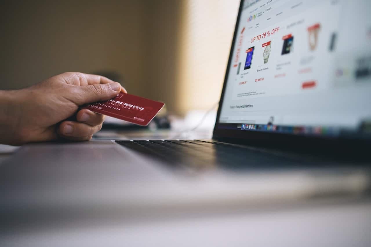 Hand holding credit card near laptop showing e-commerce website with products