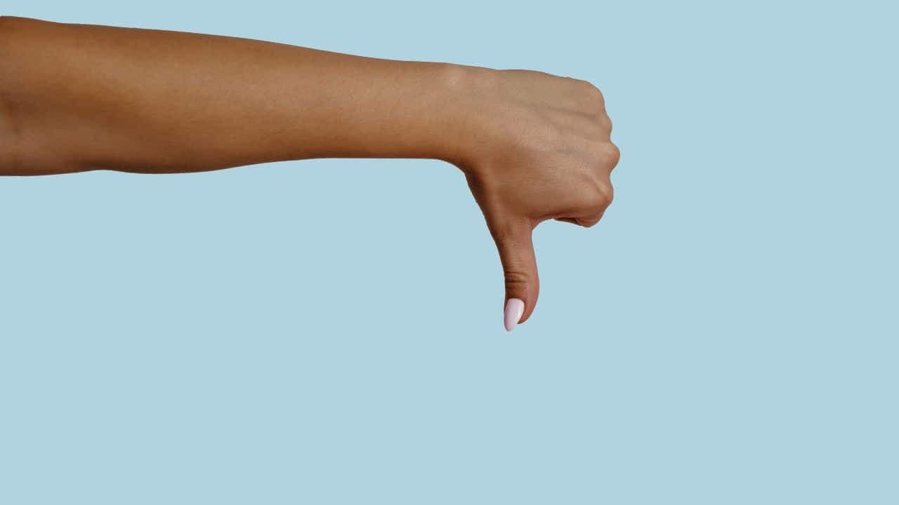 Hand making thumbs-down gesture against blue background