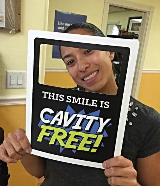 Woman in dental office holding frame prop that reads This Smile is Cavity Free