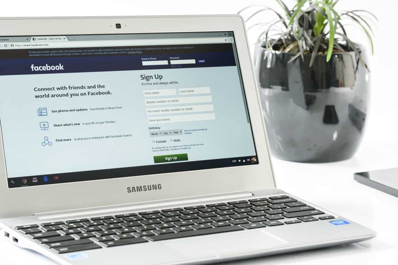 Laptop displaying Facebook signup page with potted plant in background