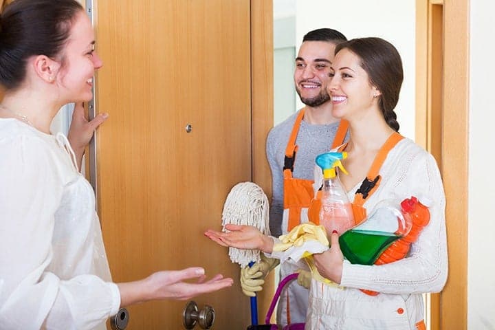 Cleaning service team in orange aprons greeting customer at home