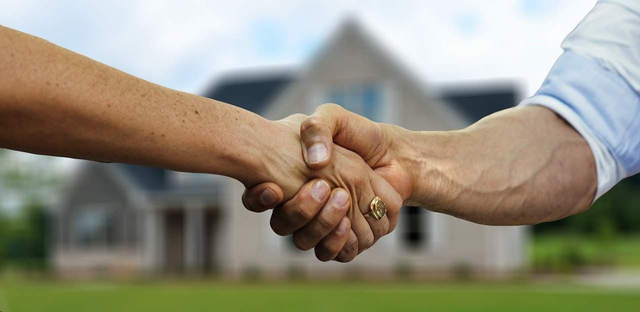 Business handshake between customer and service professional with house behind
