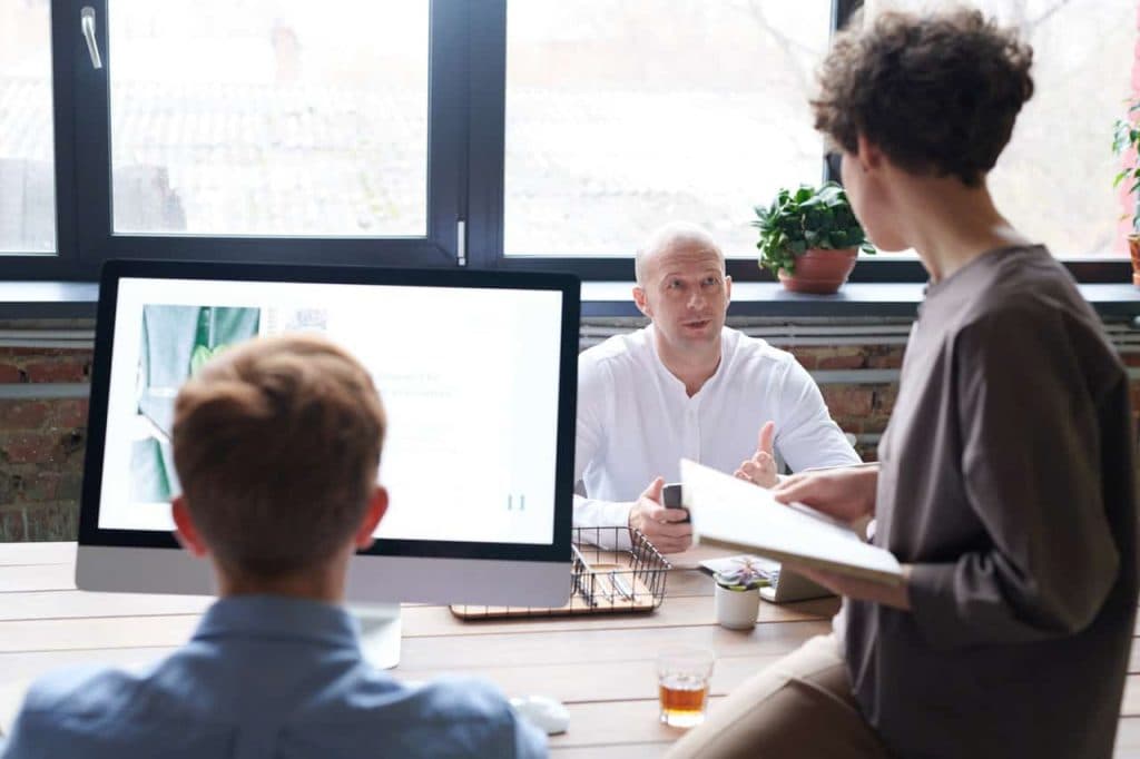 Two business professionals discussing payment solution at desk with monitor