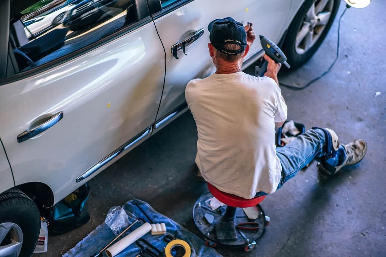 Auto technician repairing a car door dent while seated on a rolling shop stool
