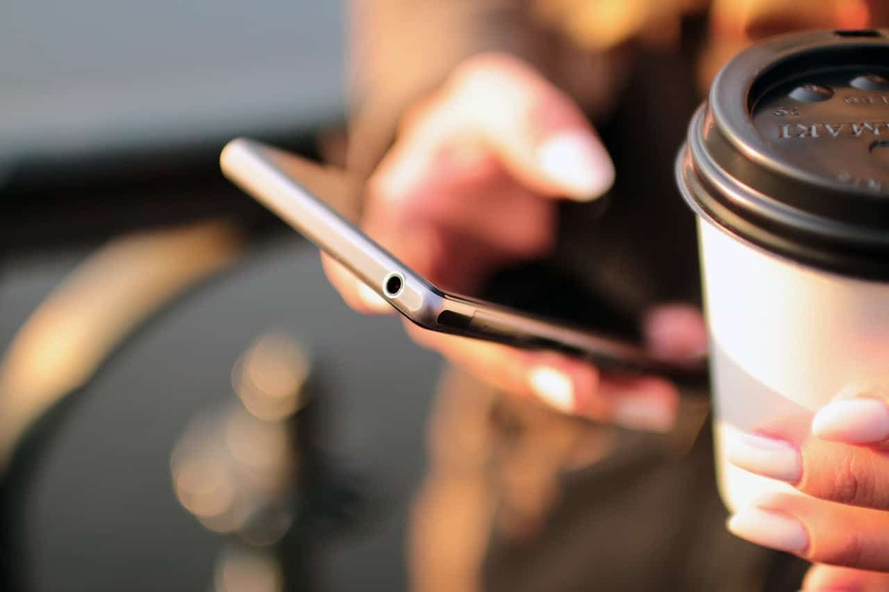 Close-up of person holding smartphone with coffee cup in background