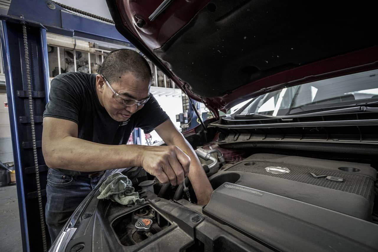 Auto technician working on vehicle engine with wrench in service bay