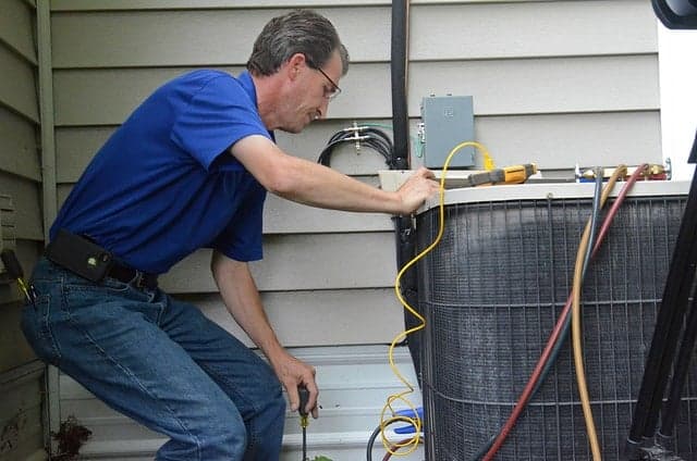 Technician servicing outdoor air conditioning unit with refrigerant lines