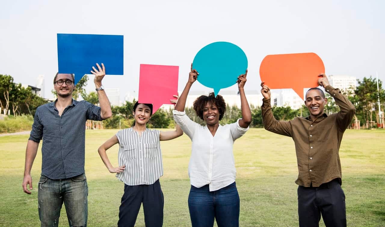 Four people holding colorful speech bubbles in outdoor field
