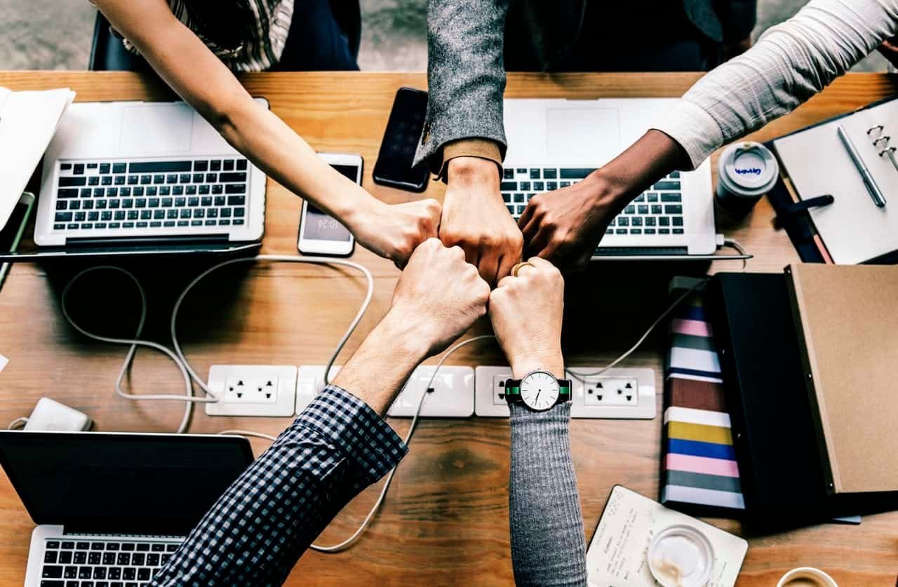 Team members fist-bumping over desk with laptops and phones