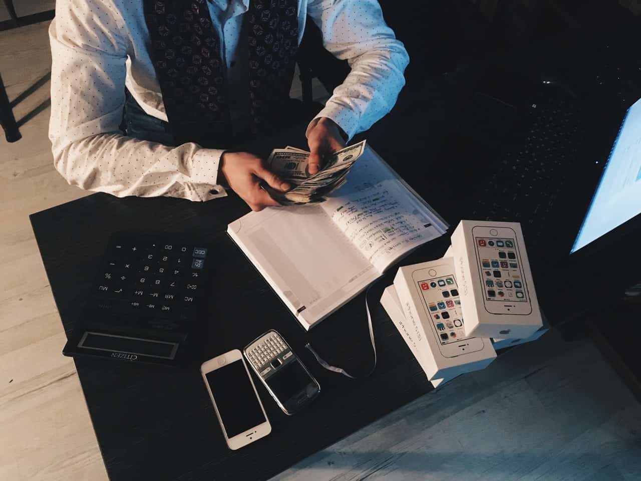 Overhead view of hands holding money and documents with calculator, notebook, and phones