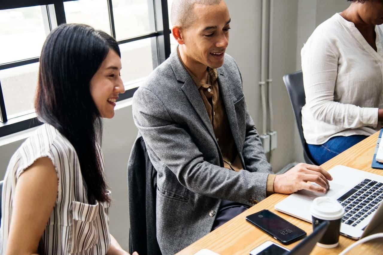 Three diverse employees smiling while working together at table with laptops and coffee