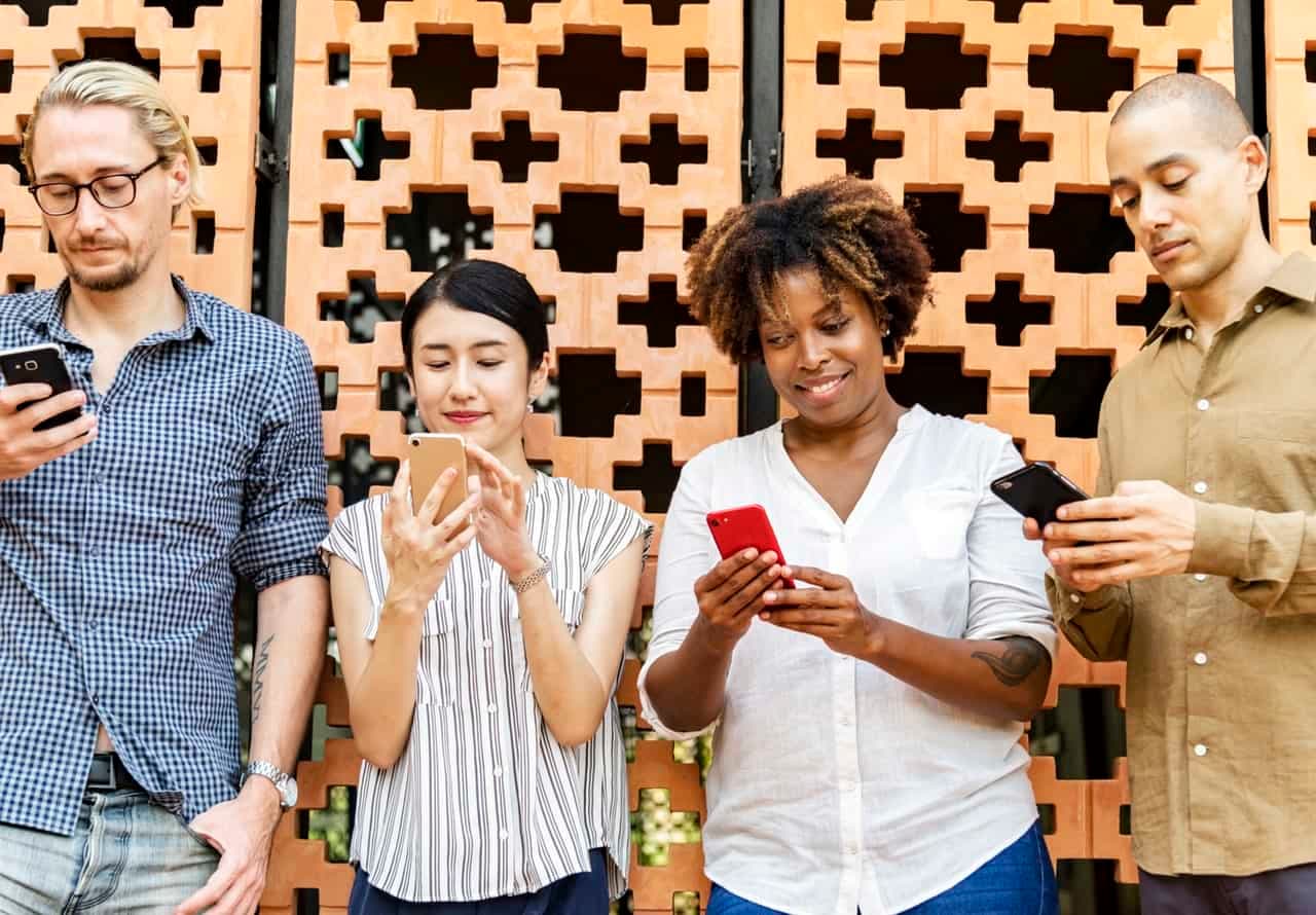Group of four diverse people looking at smartphones against brick background