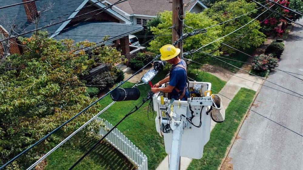 Utility worker in hard hat installing electrical cable on utility pole