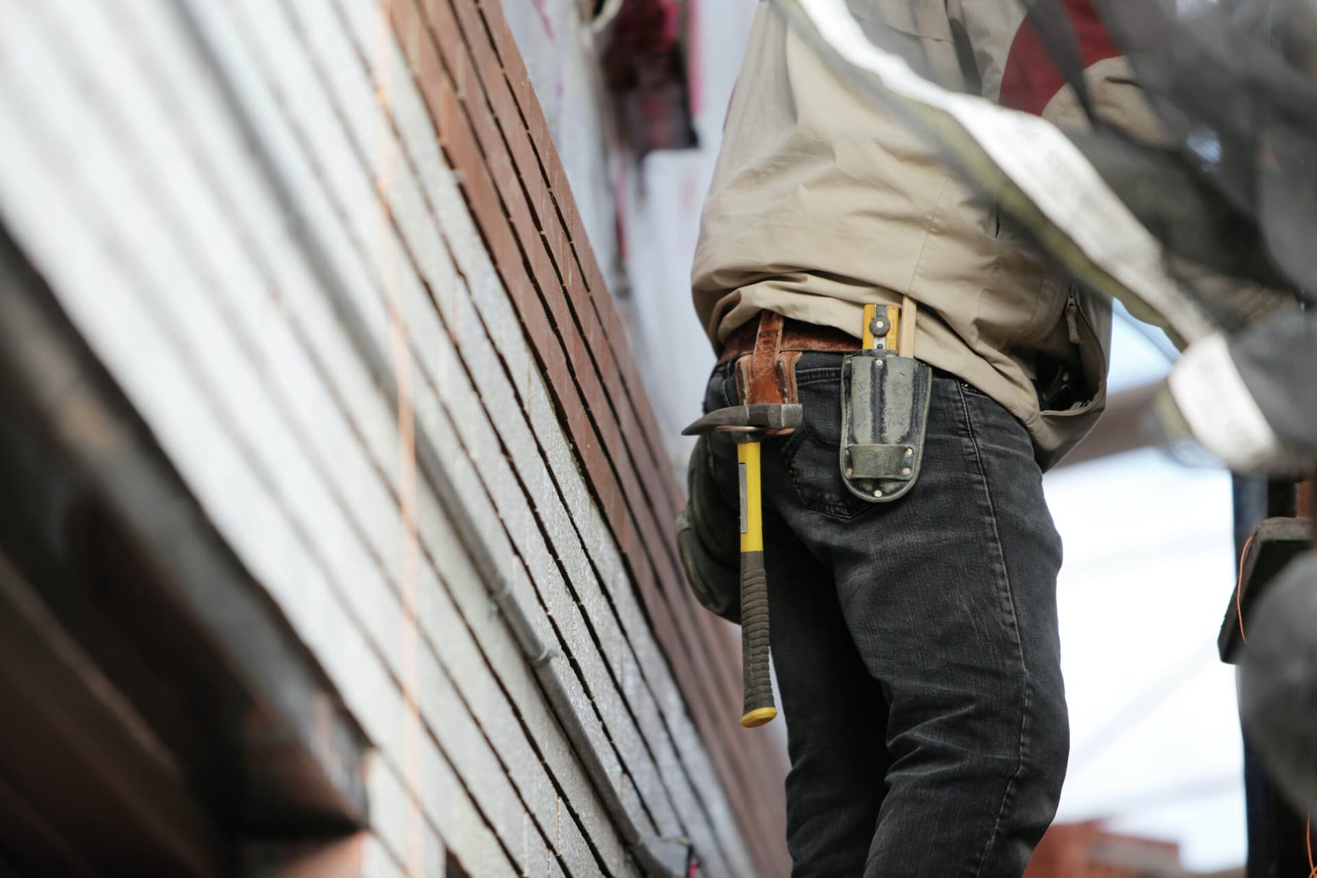 Construction worker wearing tool belt standing against brick wall