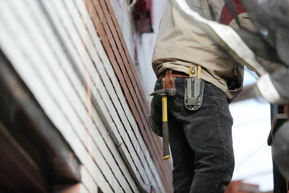 Construction worker wearing tool belt standing next to building wall