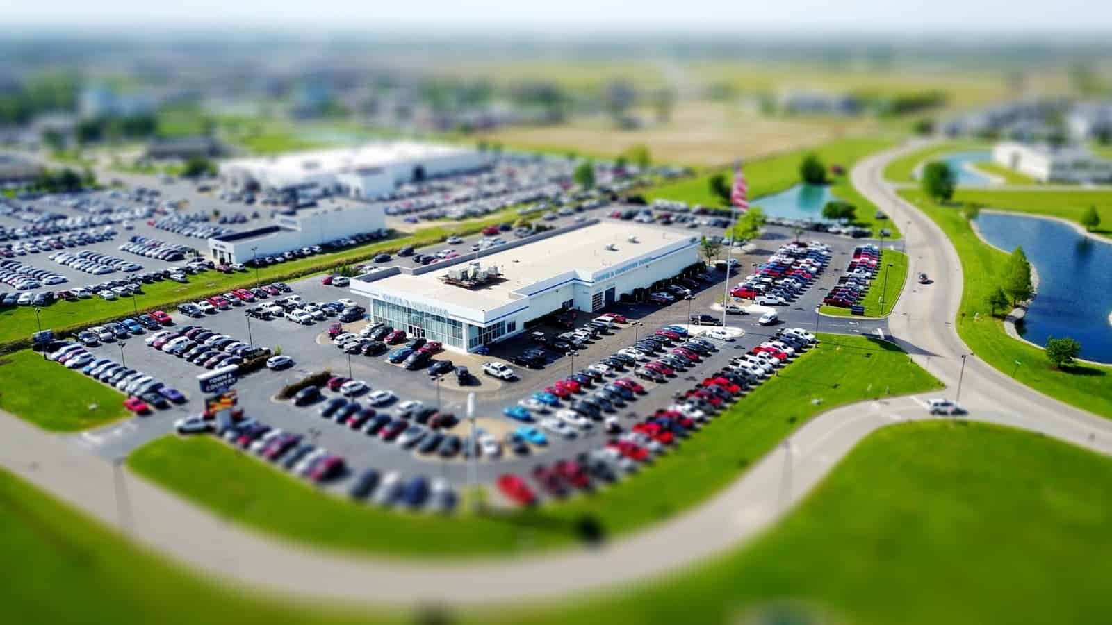 Aerial tilt-shift view of automotive dealership with showroom and parking lot