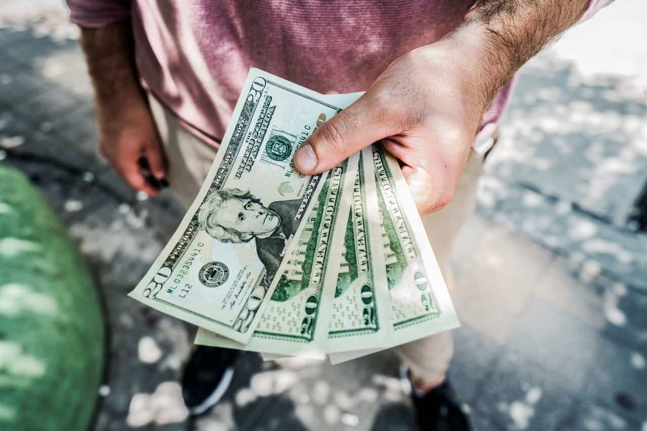 Hand holding fanned-out US dollar bills in outdoor setting