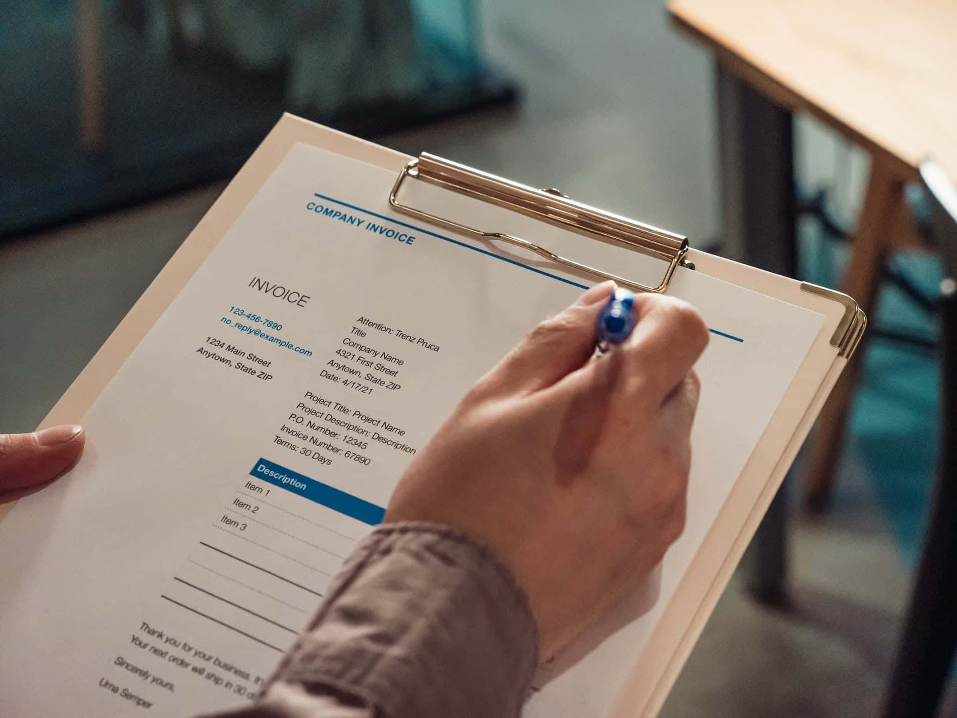 Hands holding clipboard with company invoice document and pen for business paperwork