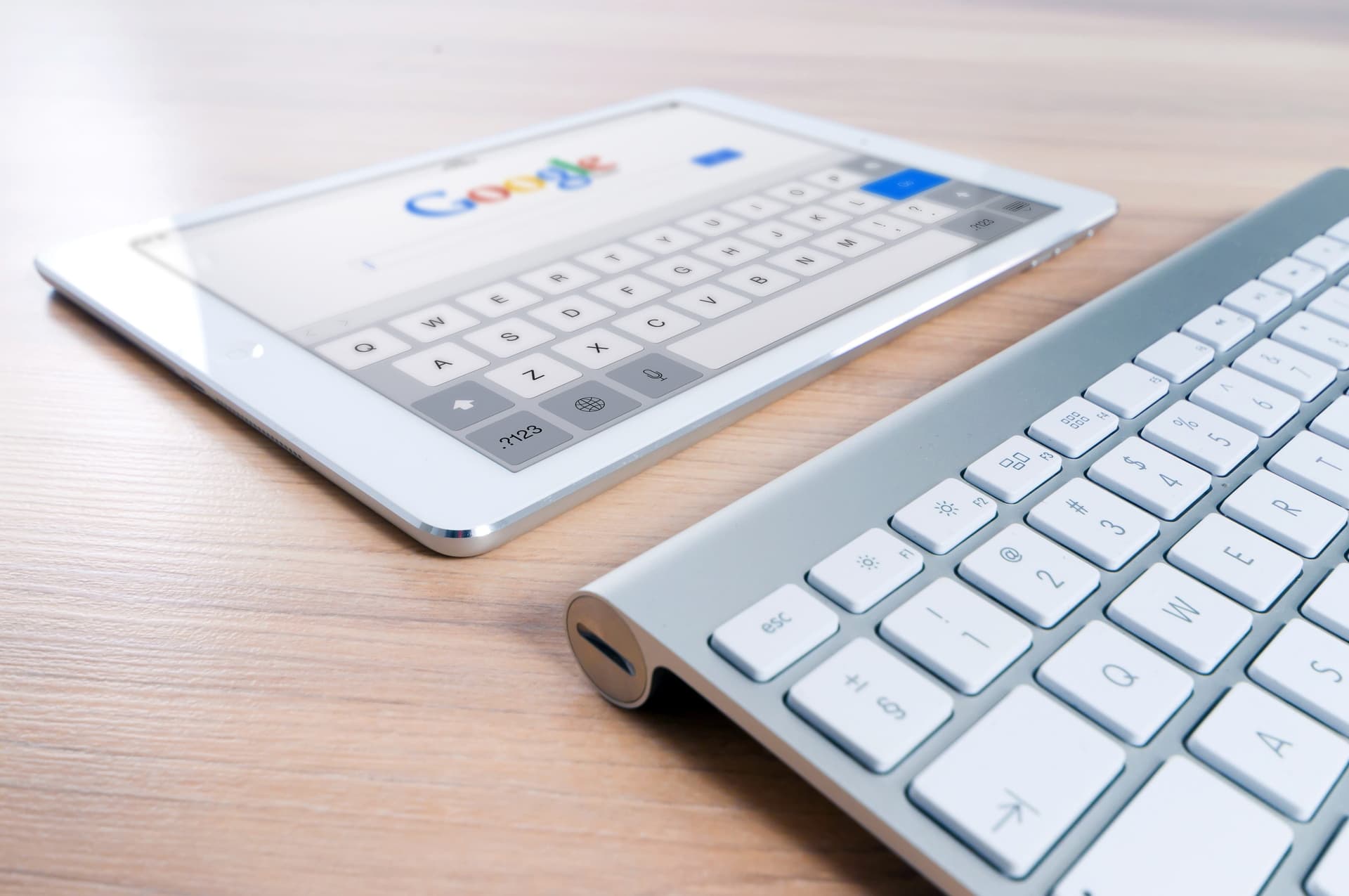 iPad displaying Google search page next to keyboard on wooden desk