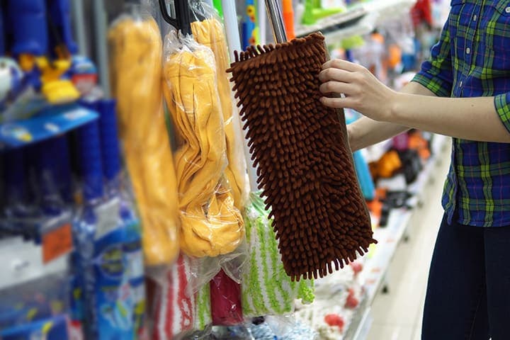 Person selecting brown dust mop from cleaning supply store shelf