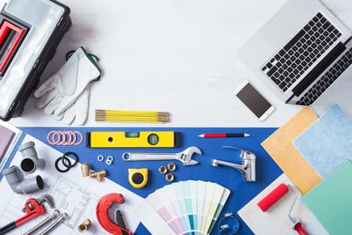 Overhead workspace with laptop, tools, paint color swatches, level, wrench, and construction equipment on blue surface