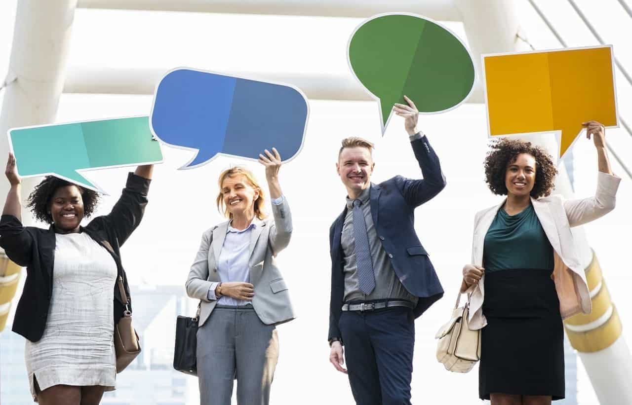 Four business professionals holding colored speech bubbles in turquoise, blue, green, and yellow against white background