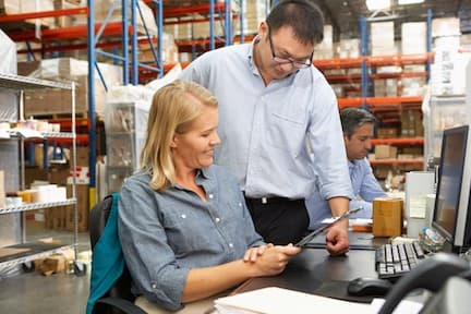 Man and woman reviewing tablet in warehouse with industrial shelving