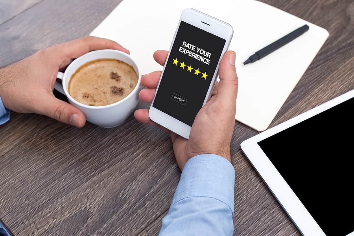 Person holding coffee and phone with rate your experience five-star prompt