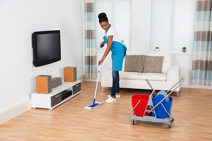 Professional cleaner mopping hardwood floor with mobile cleaning cart