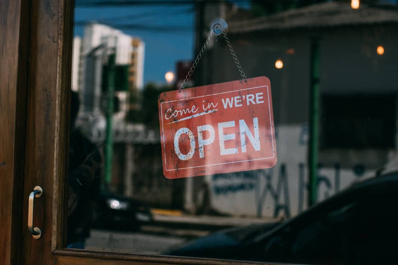 Red neon Come in We're Open sign hanging on storefront window at night