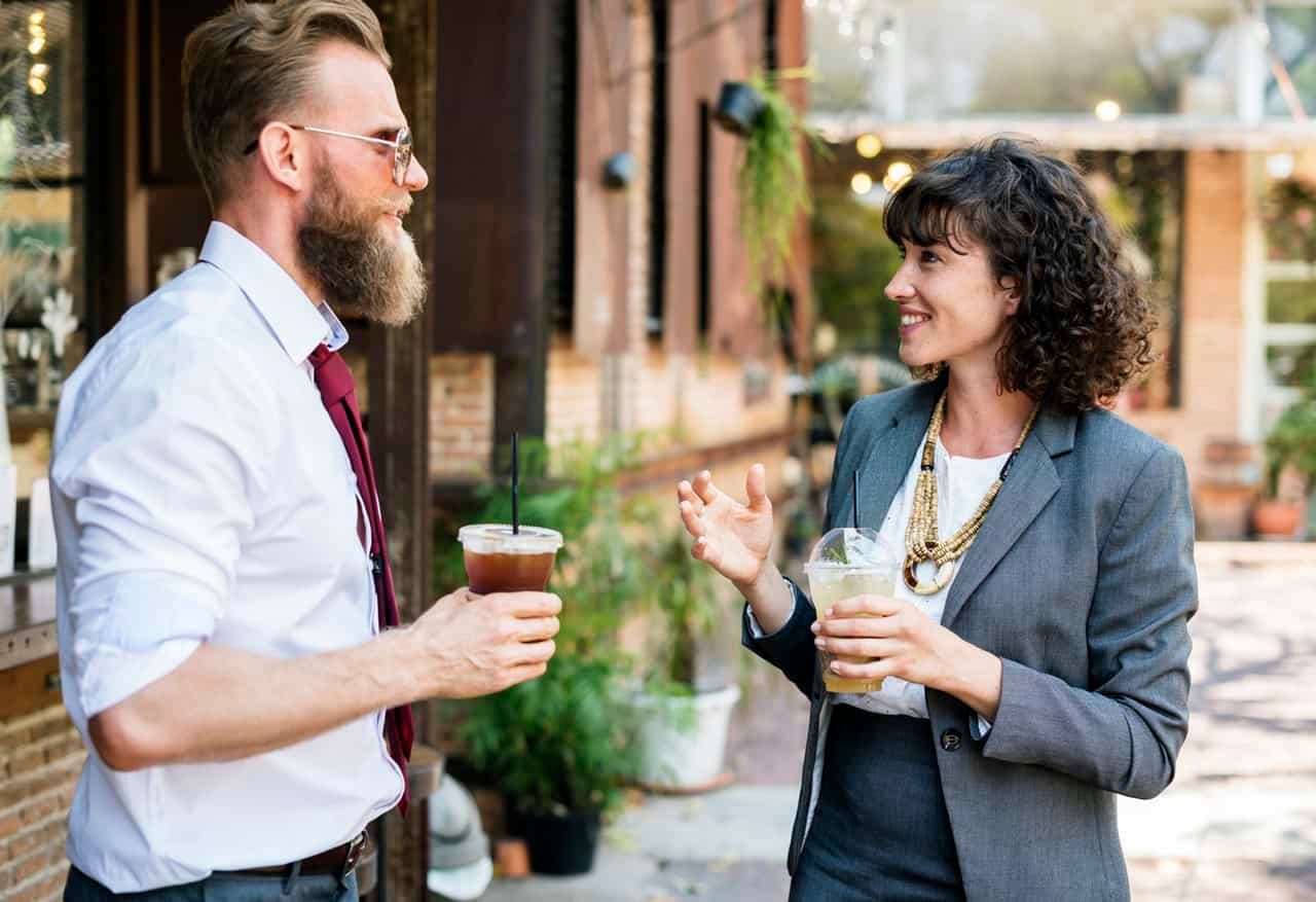 Two professionals in business attire conversing outdoors with beverages