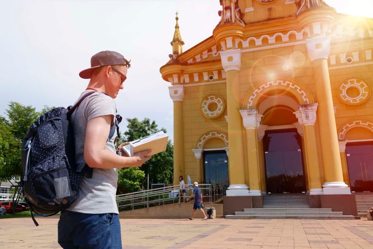 Traveler with a backpack and guidebook standing in front of an ornate yellow church