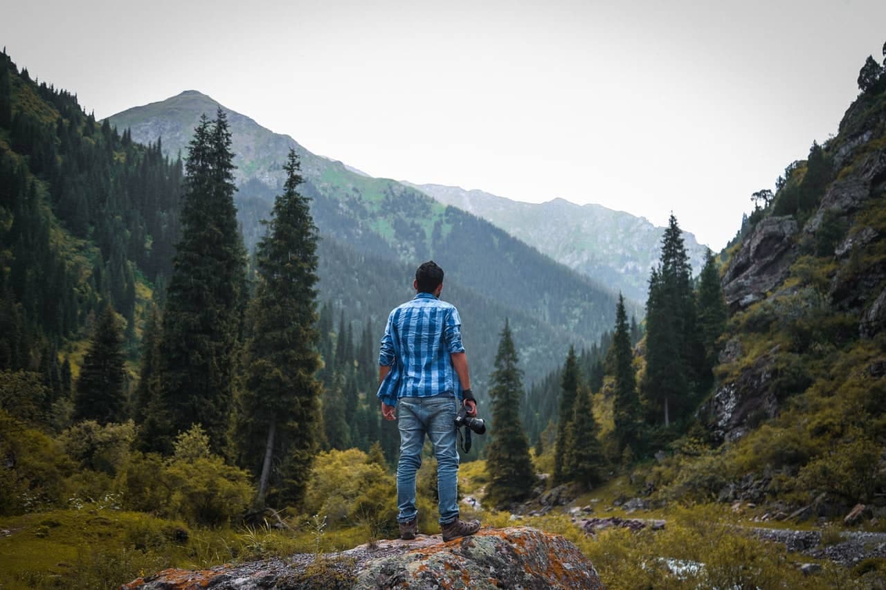 Photographer standing on a rock, back to camera, overlooking a forested mountain valley