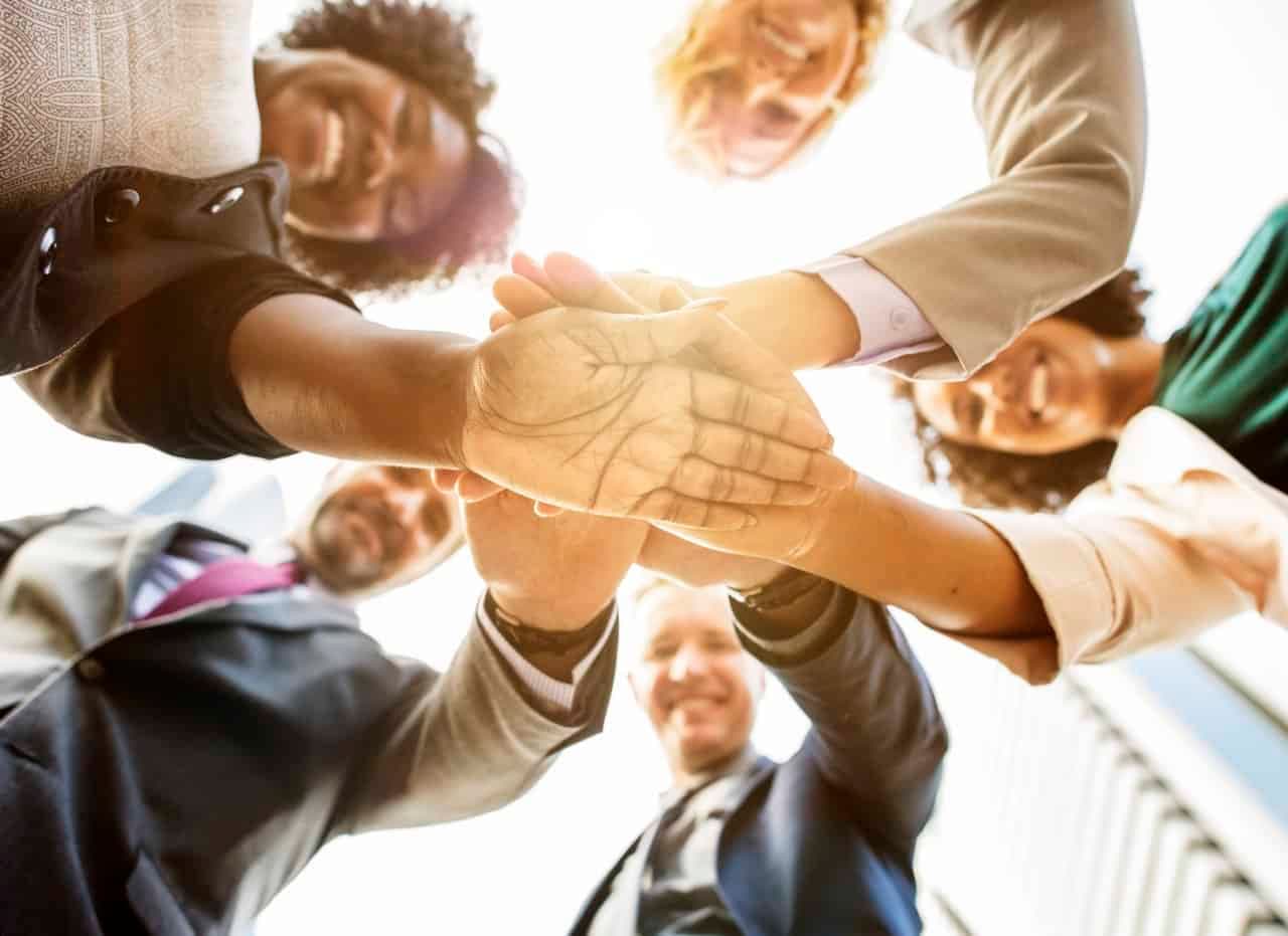 Businesspeople's hands joined together, seen from below looking up at their smiling faces