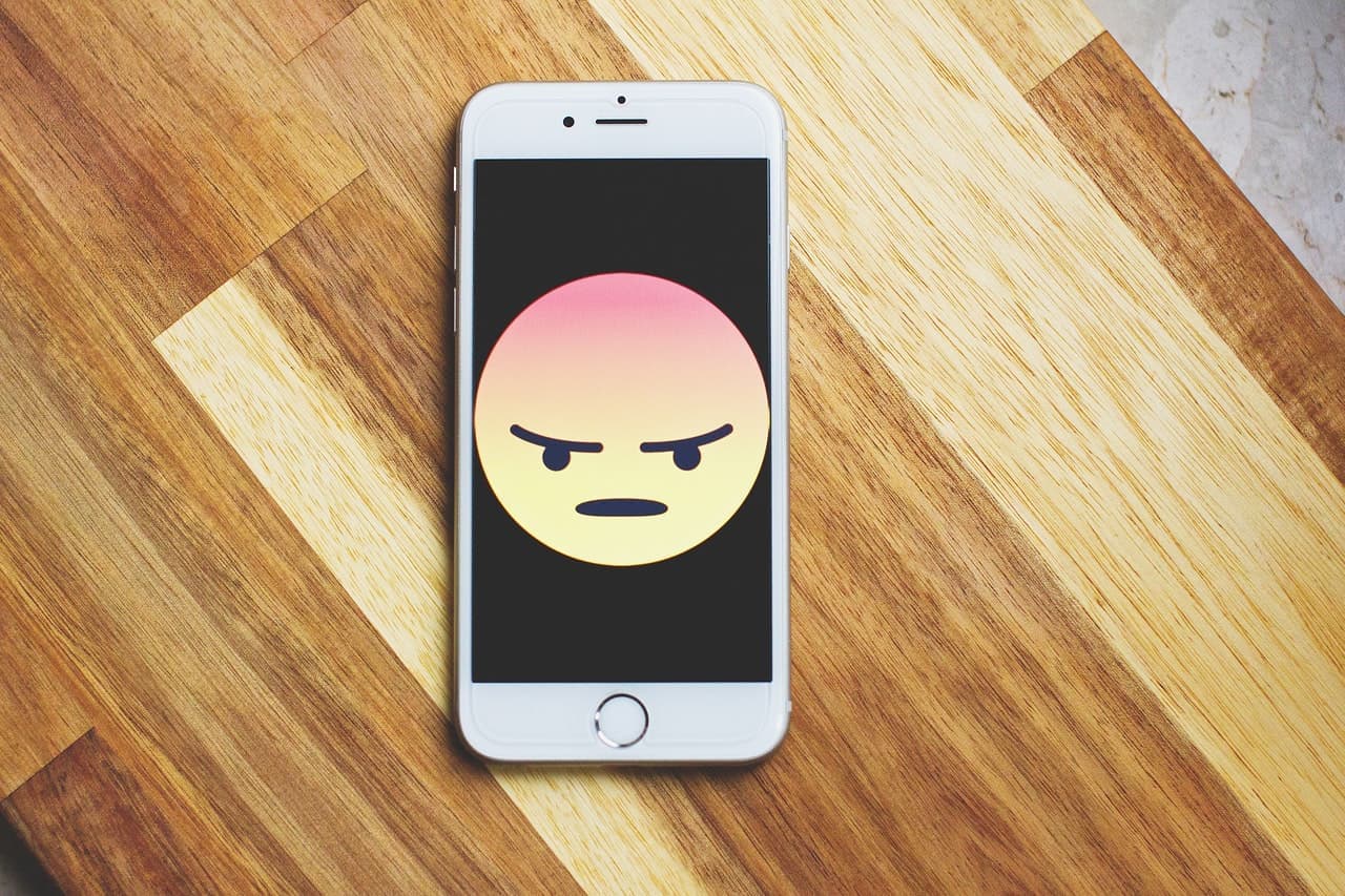 White smartphone on wooden surface displaying angry face emoji