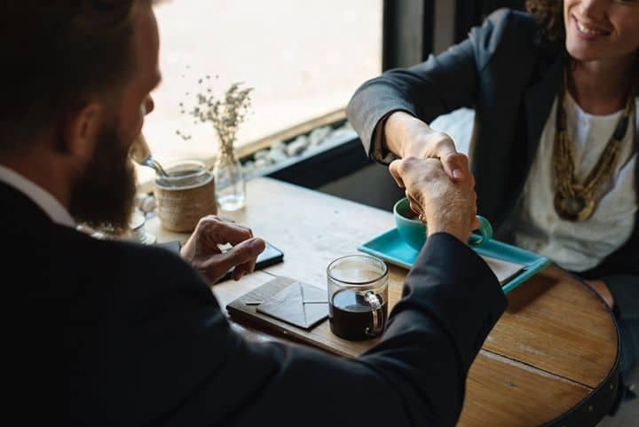Two professionals shaking hands over coffee at a small cafe table