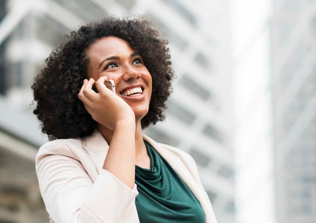 Woman on phone call smiling in business attire with blurred city buildings in background