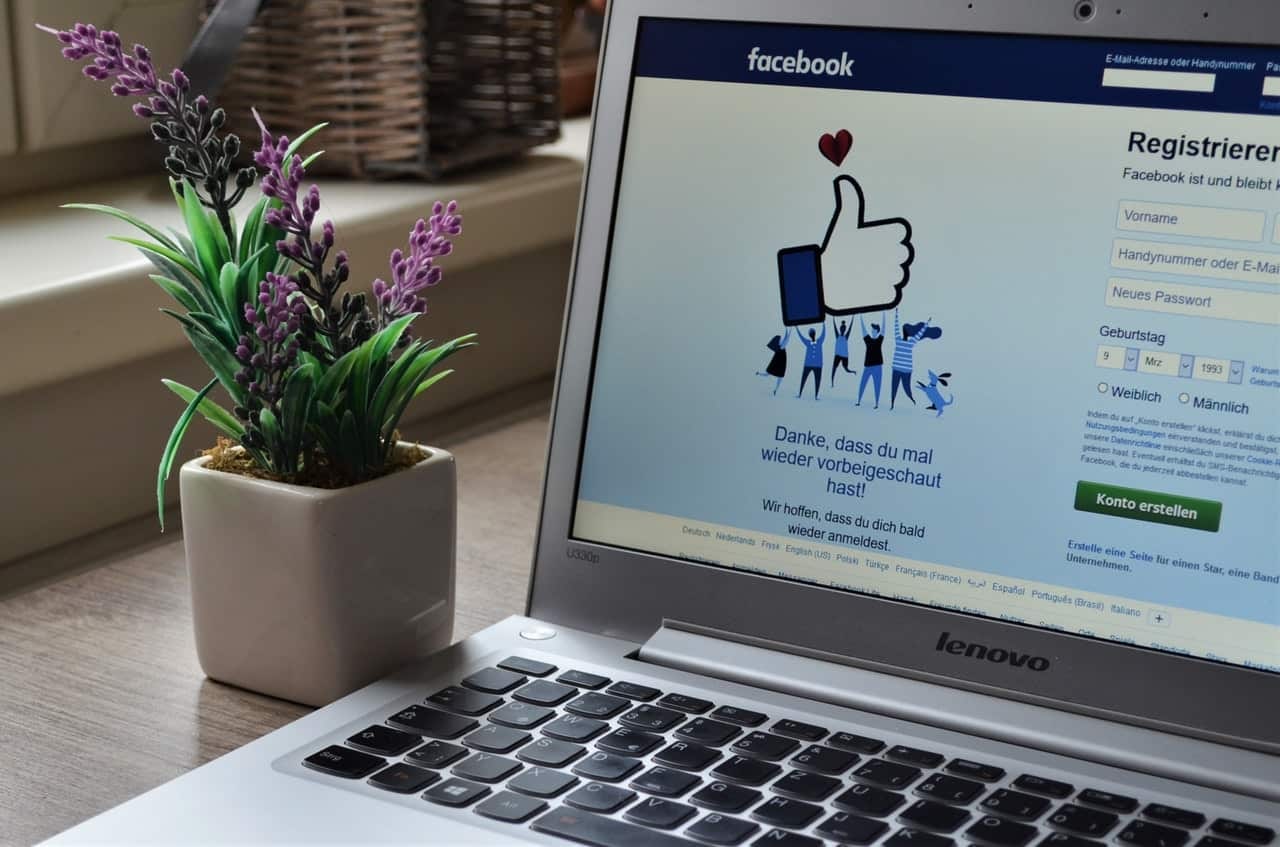 Laptop showing Facebook sign-up page with thumbs-up graphic and purple plant