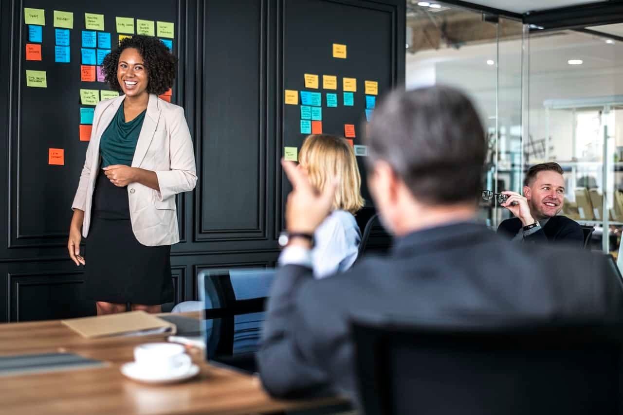 Woman presenting to colleagues with colorful sticky notes on wall board behind her