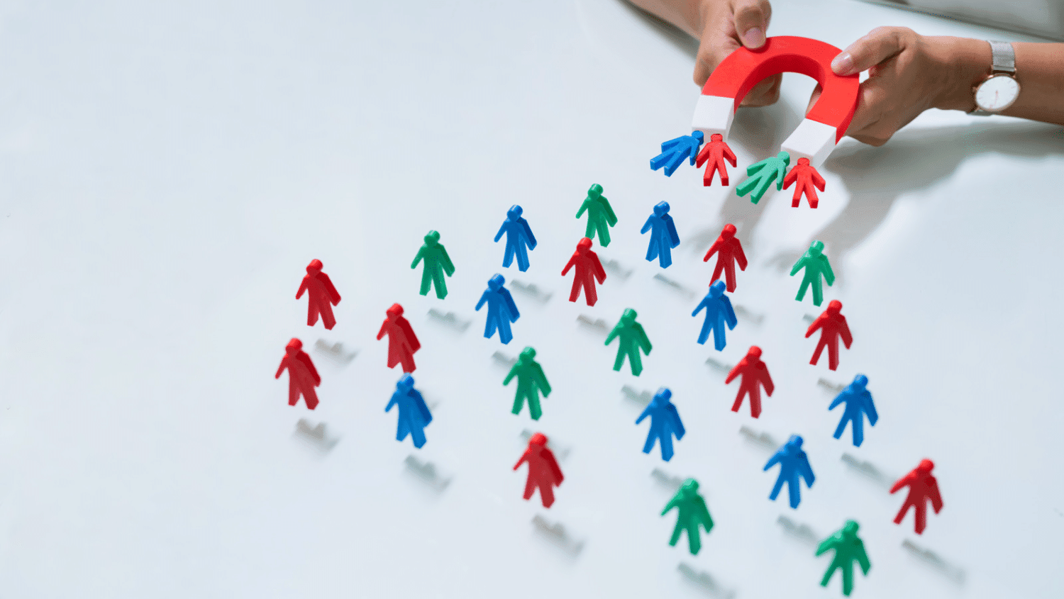 Hand holding a red horseshoe magnet drawing in small red, blue, and green toy figures