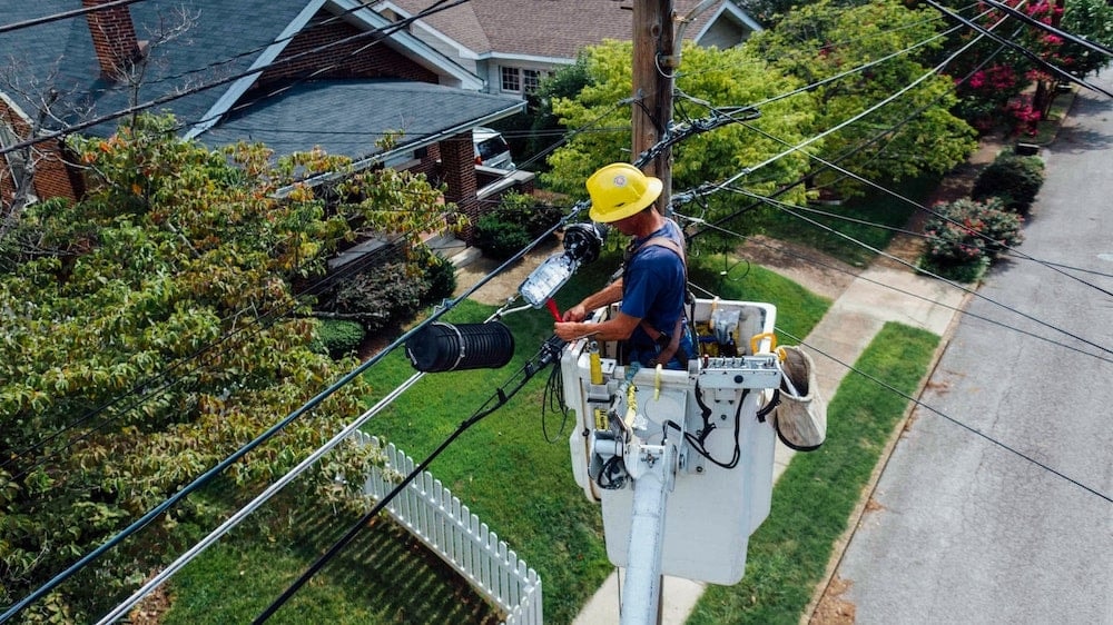 Utility worker in hard hat installing electrical cable on utility pole