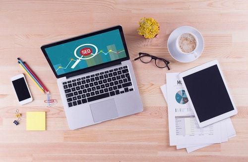 Overhead workspace view with laptop showing SEO icon and papers