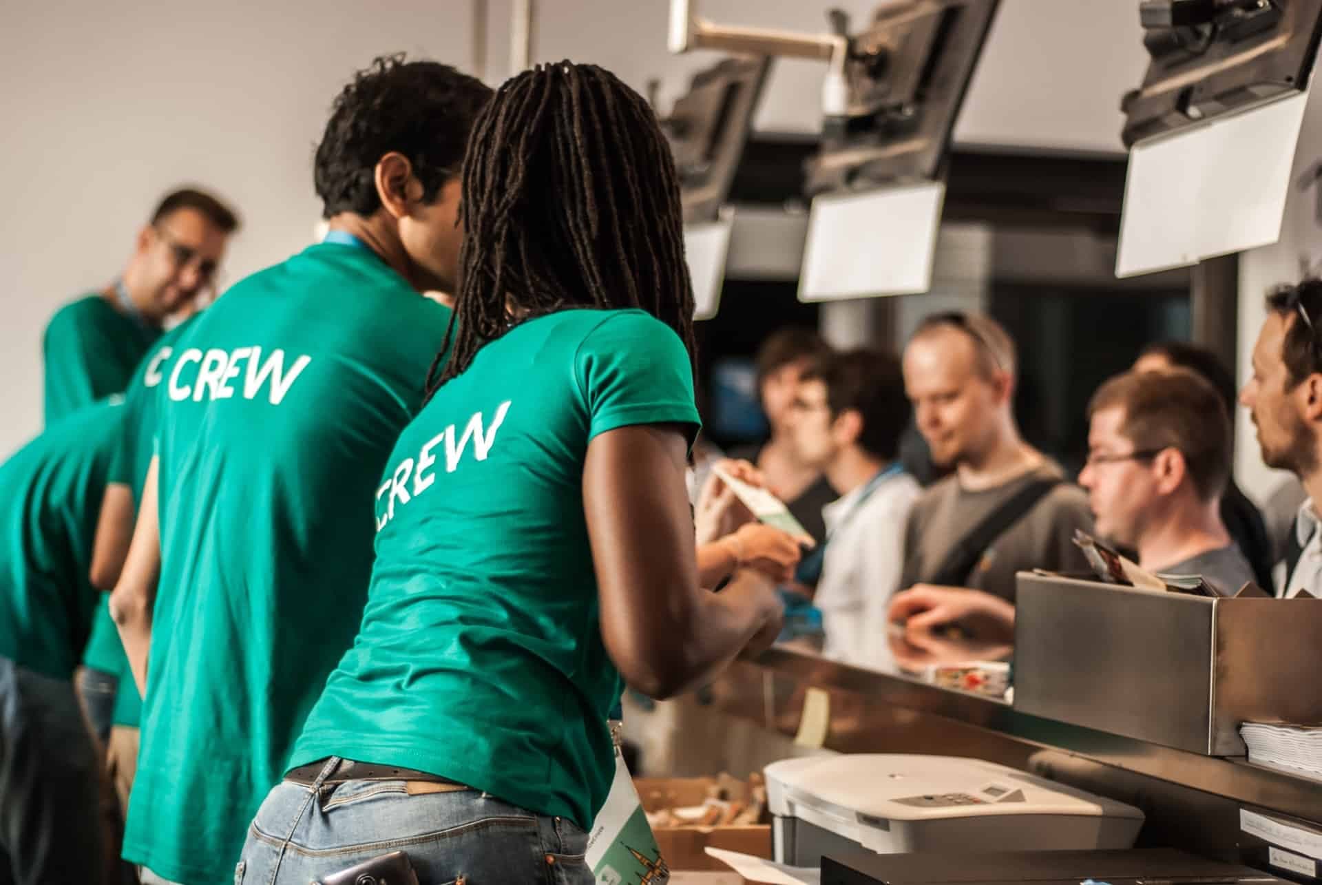 Team members in green CREW shirts serving customers at food counter